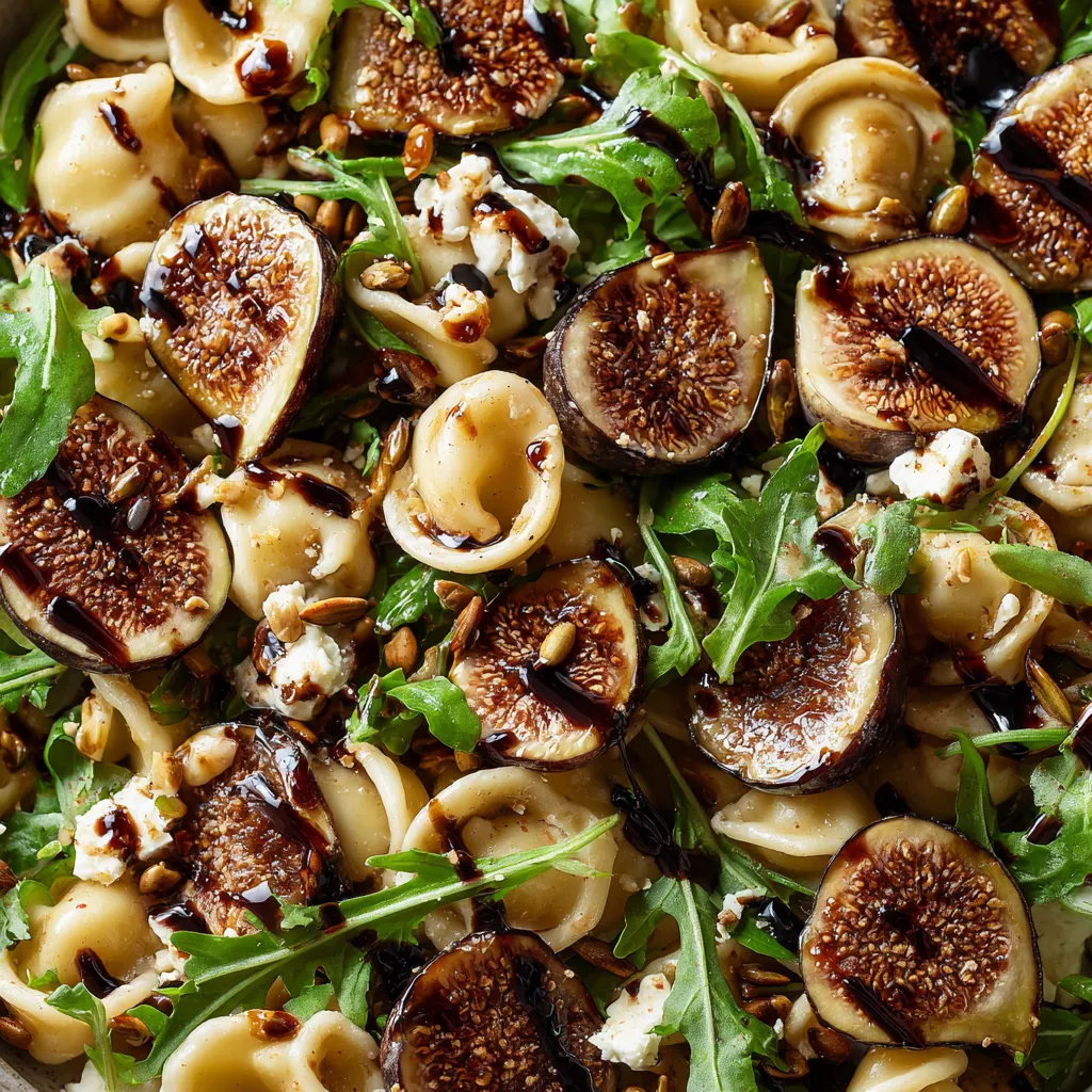 A dish of pasta salad with figs, goat cheese, arugula, and balsamic glaze.