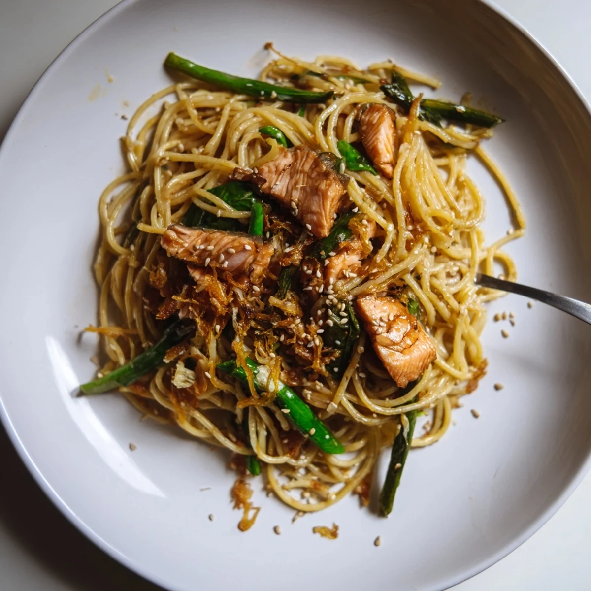 Pan-fried salmon pasta garnished with scallions and sesame seeds, bursting with umami flavors.