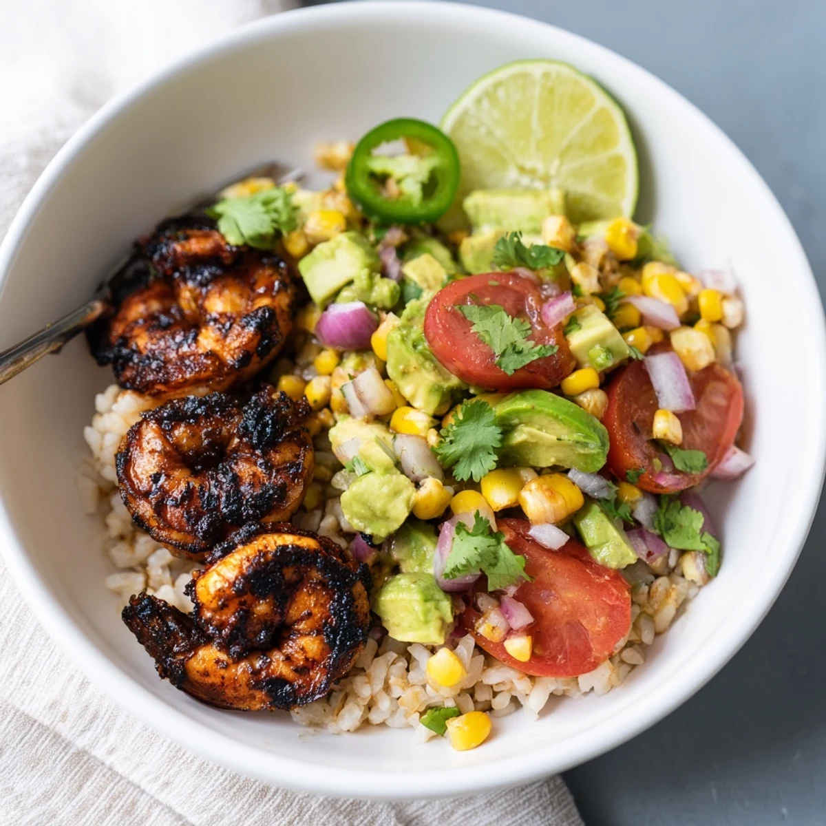 Savory blackened shrimp bowl featuring zesty avocado corn salsa and lime wedges.  