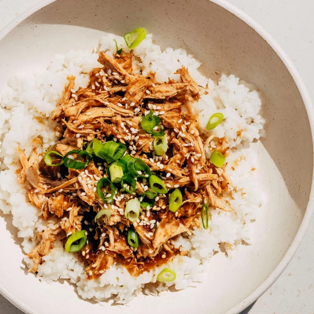 A steaming bowl of comforting teriyaki chicken over rice, garnished with green onions; a delightful aroma.