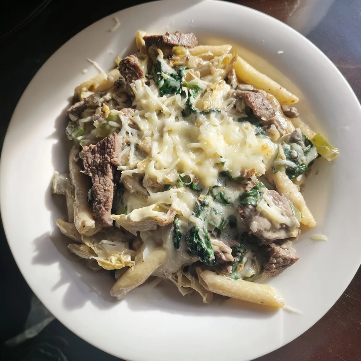 A close-up view of a savory Steak & Spinach Artichoke Pasta Bake, ready to serve with a crusty bread.
