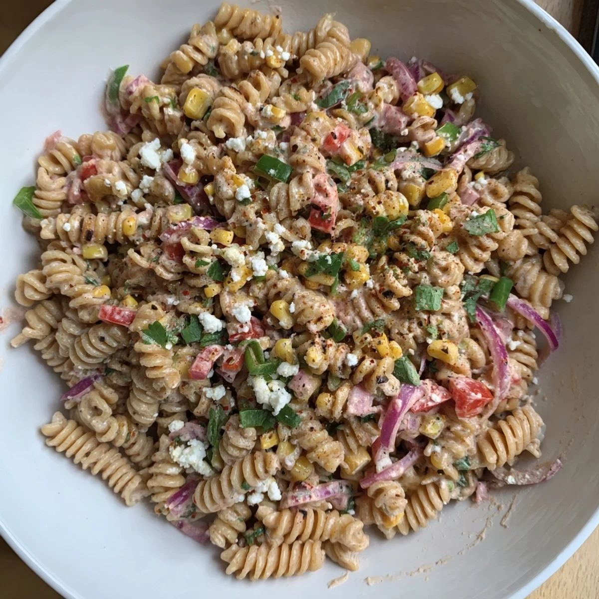 A colorful bowl of Healthier Mexican Street Corn Pasta Salad showcases charred corn and creamy dressing.