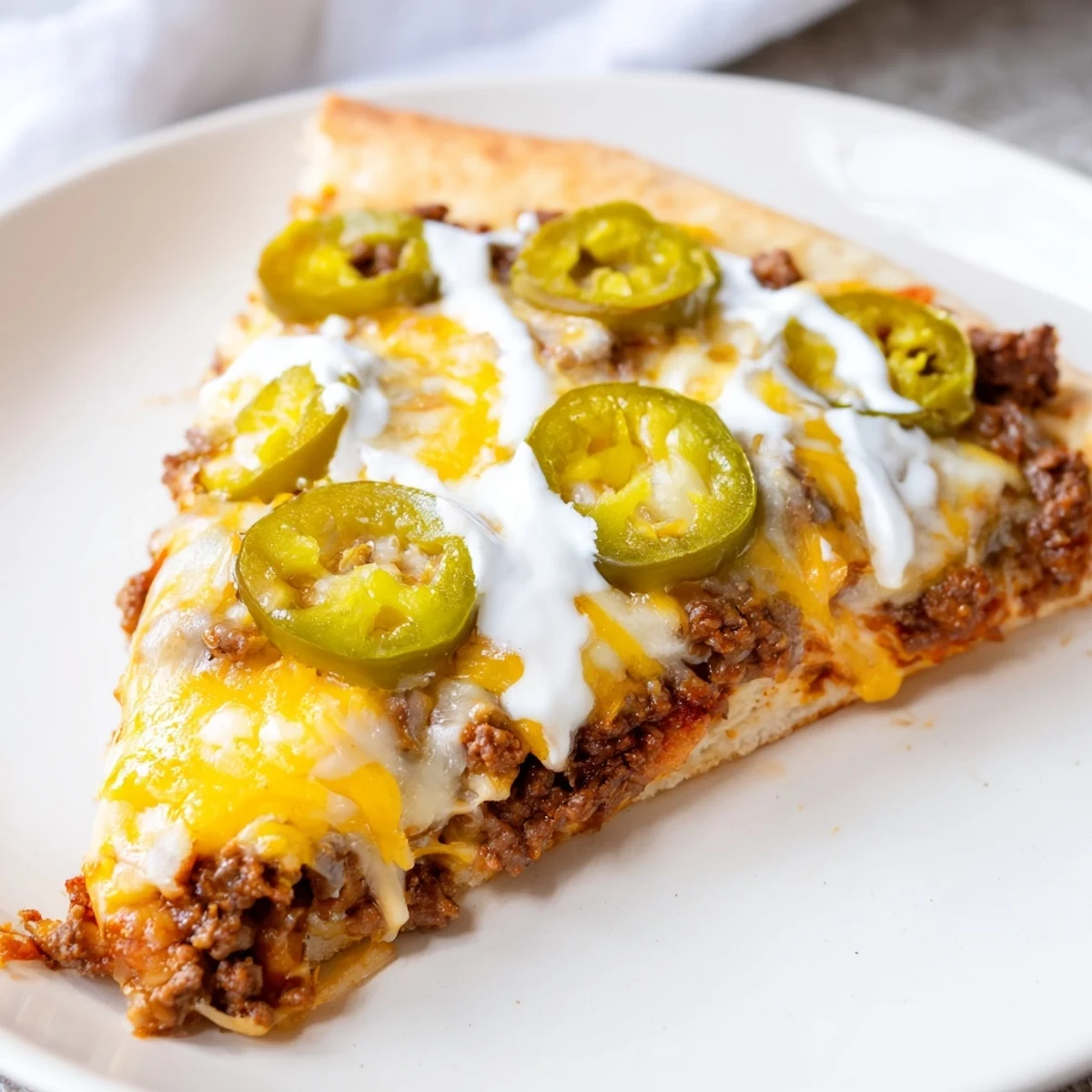 Golden-crusted ground beef taco pizza, perfect for a family dinner with a creamy drizzle on top.