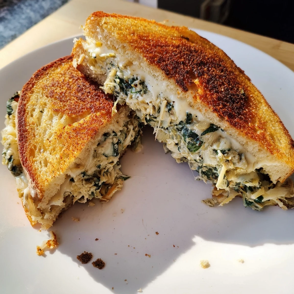 Golden-brown spinach artichoke grilled cheese, oozing with melted cheese, ready to be enjoyed.