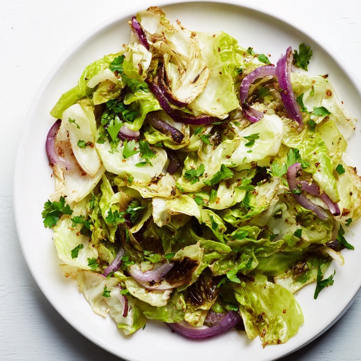Steaming sautéed cabbage with garlic and Mediterranean spices fills the skillet with golden edges and vibrant red onion slices.  