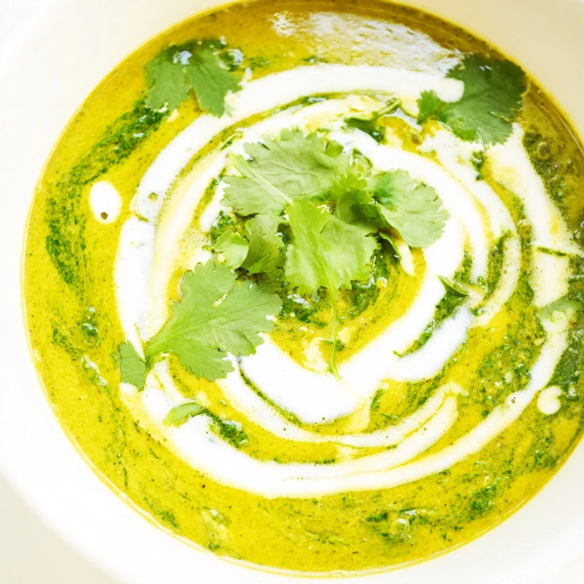 Close-up of a silky Spinach Coriander Lemongrass Soup with coconut milk base, topped with a sprinkle of fresh herbs.