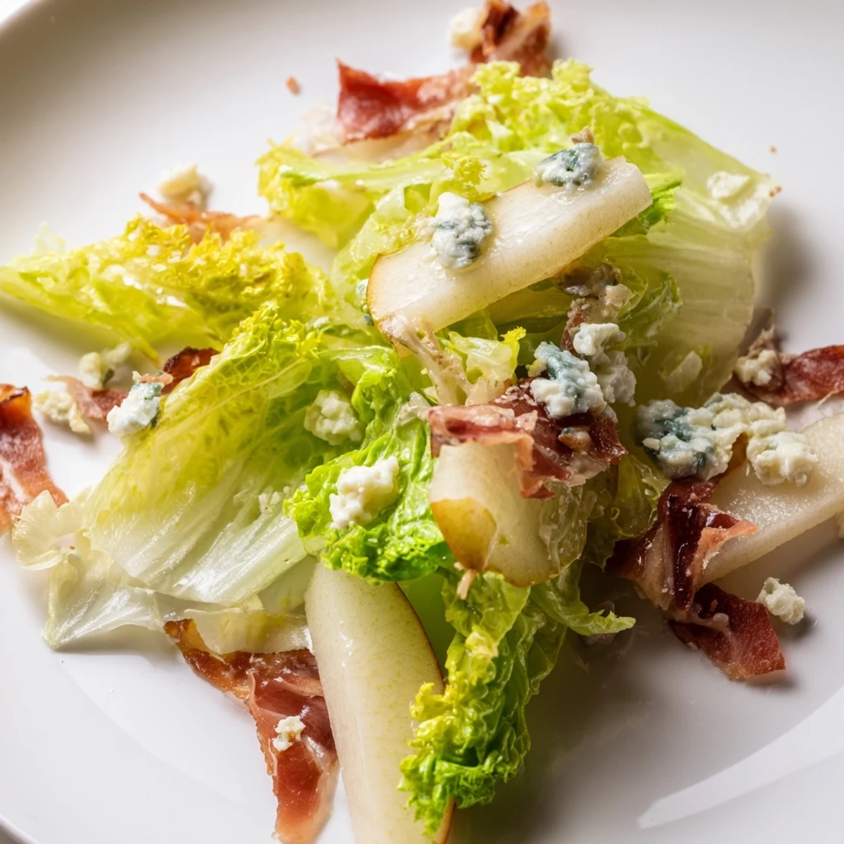 Close-up of Frisée, Pear, Blue Cheese, and Crispy Prosciutto Salad topped with creamy blue cheese crumbles and toasted walnuts on a wooden board.