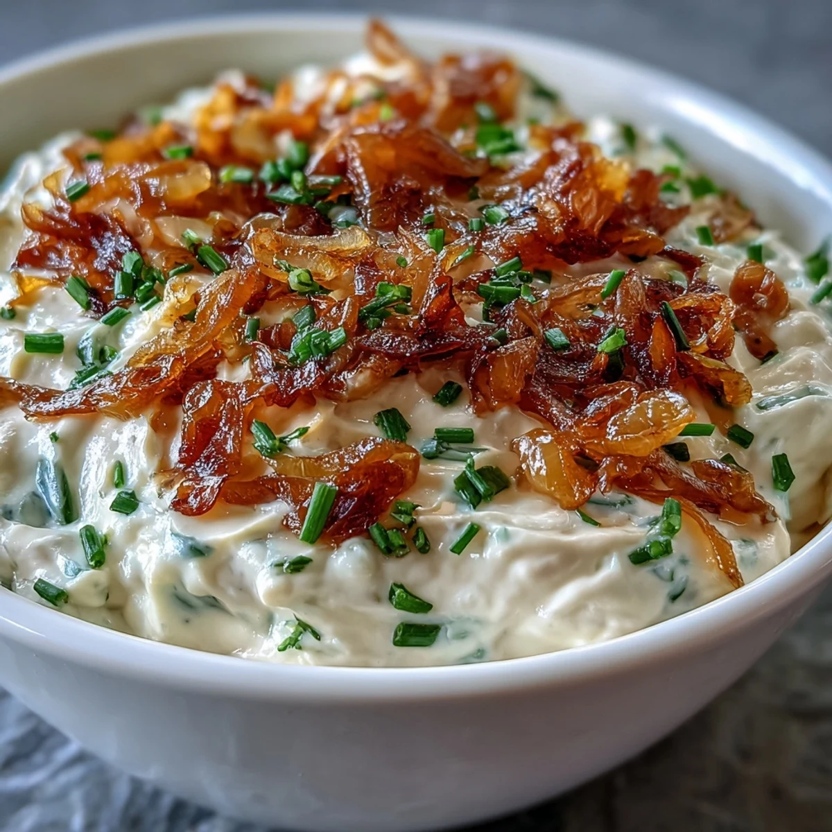 Golden caramelized onions blend into tangy sour cream dip, garnished with bright green chives for a savory appetizer.  