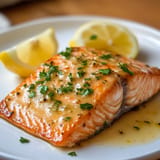A plate of salmon with lemon wedges on top.