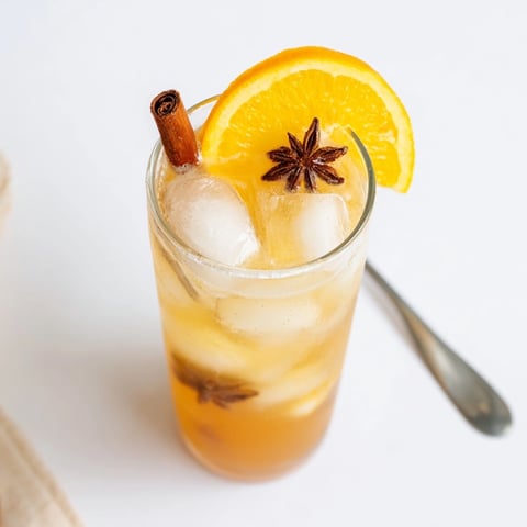 Icy Cinnamon-Spiced Chai Fizz in a fancy glass, garnished with orange and spice.