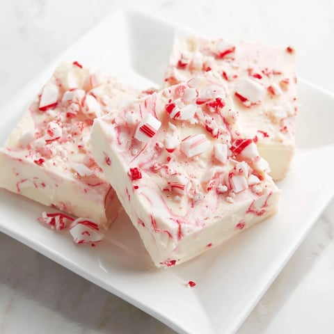 A close-up of White Chocolate Peppermint Bark Fudge glistening with crushed candy cane topping.