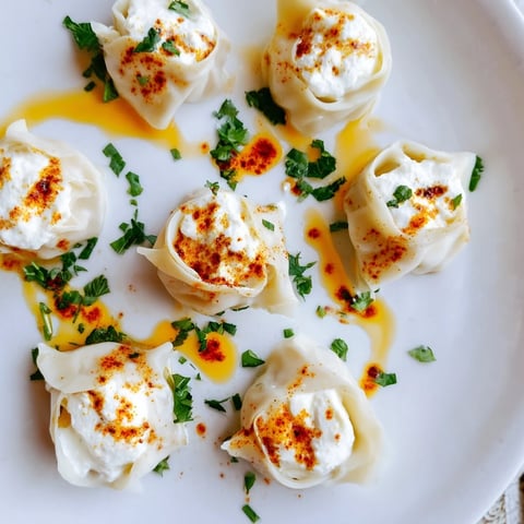 A close-up shot of steaming Turkish cheesy manti, topped with spiced butter and yogurt.