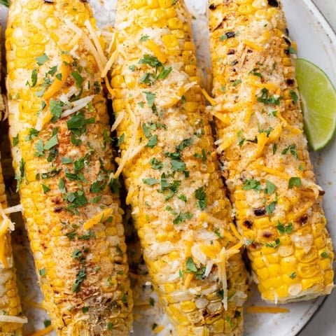 Golden, cheesy corn ribs fresh from the oven, ready for a flavorful bite with lime wedges.