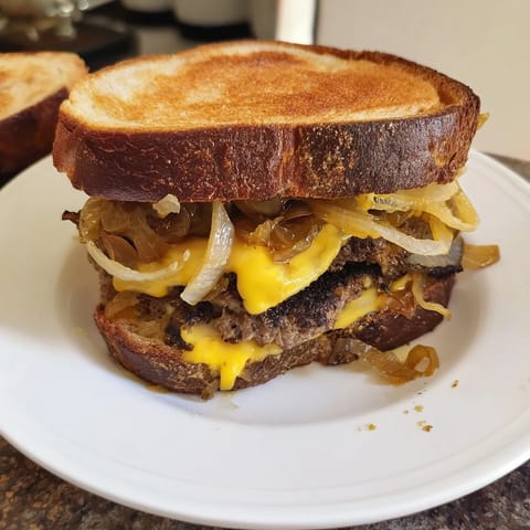 A close-up shot of a classic patty melt skillet with melted Swiss cheese oozing, a tasty meal.