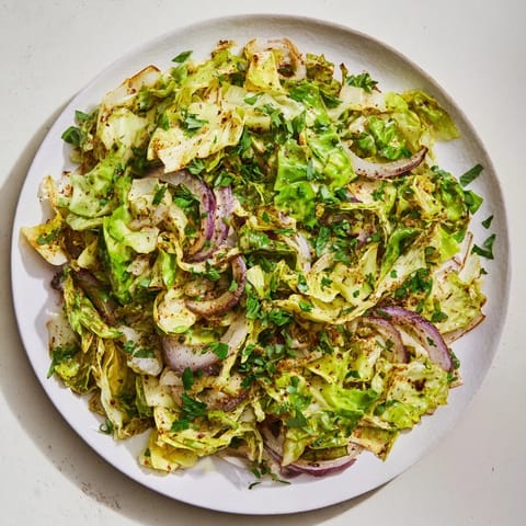 A close-up of sautéed cabbage with garlic and Mediterranean spices, garnished with fresh parsley and lemon wedges for serving.  