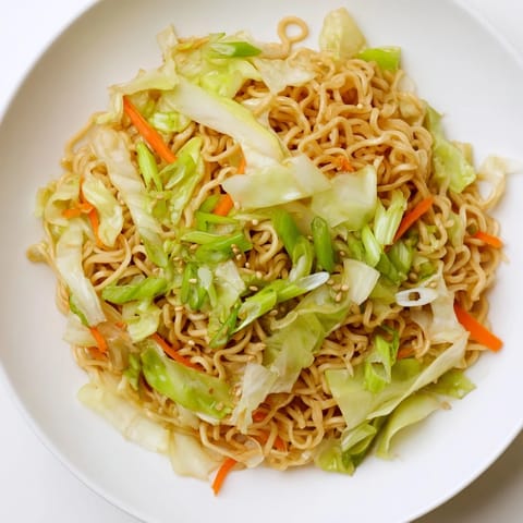 Close-up of Fried Cabbage Ramen in a wok, garnished with scallions and sesame seeds.  