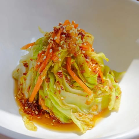 Vibrant bowl of Hot and Sour Cabbage garnished with scallions and sesame seeds, ready to serve as a zesty vegan side dish alongside steamed rice.