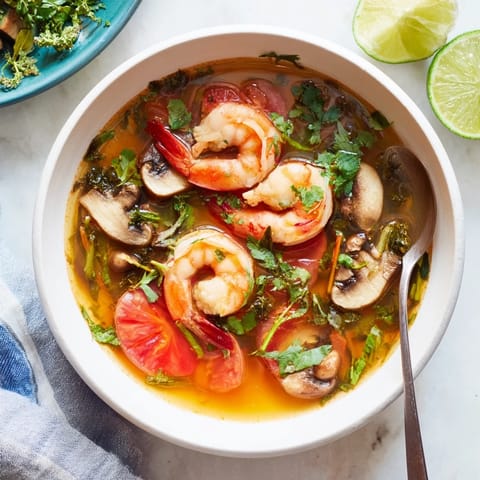 Spicy and sour Tom Yum Soup with tomatoes and Thai herbs, steaming in a rustic pot.