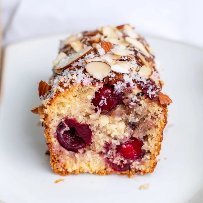 A beautifully browned Cherry Almond Loaf Cake, sliced and ready to serve with coffee for brunch.