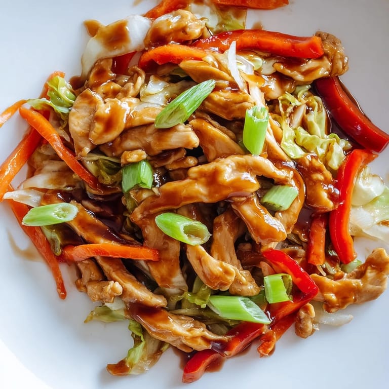 A close-up of colorful Chicken Cabbage Stir-Fry with vibrant red peppers, carrots, and green onions in an aromatic garlic-ginger glaze.  