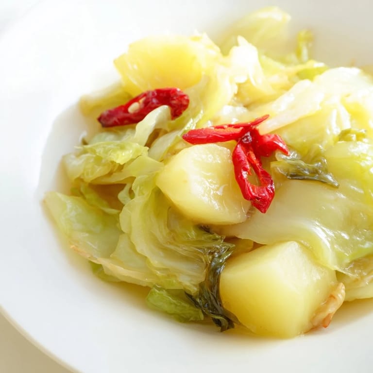 Hearty braised cabbage with potatoes and chili, garnished with fresh parsley and a bright lemon wedge.
