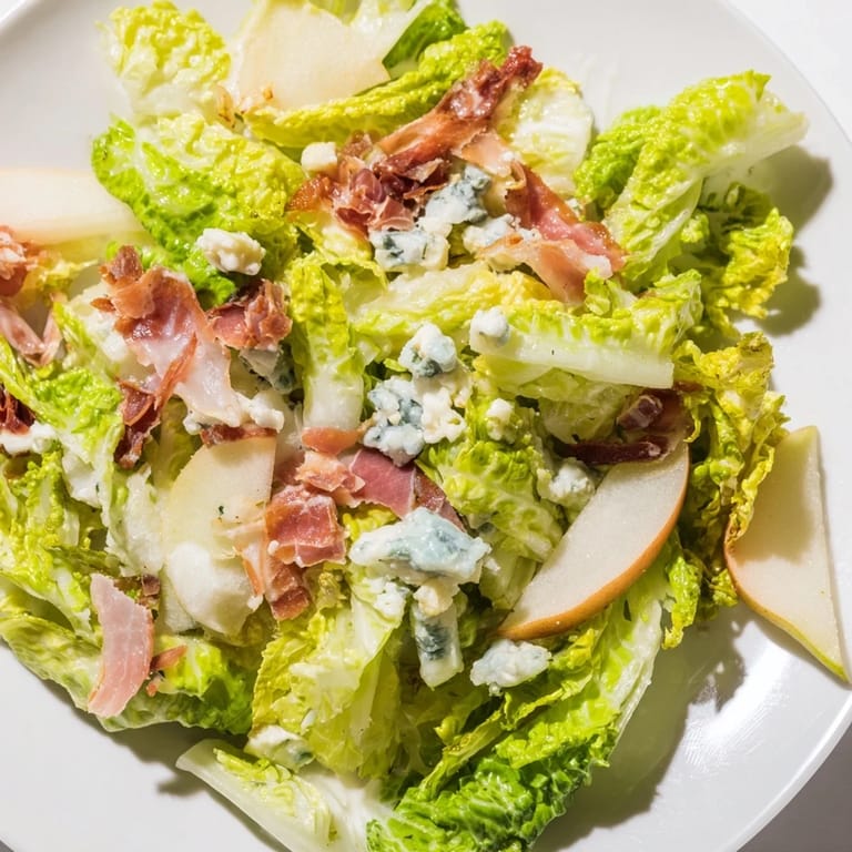 Elegant plated Frisée, Pear, Blue Cheese, and Crispy Prosciutto Salad drizzled with tangy vinaigrette, served with white wine as a light lunch.