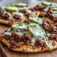Crispy mini naan bases loaded with seasoned ground beef, melted cheese sauce, and tangy dill pickle slices for a savory bite. These Cheeseburger Garlic Naan Pizzas make the ultimate easy weeknight dinner or game day snack, served warm and gooey right from the oven.