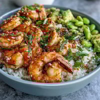Fresh shrimp poke bowl with juicy mango, edamame, and avocado, drizzled with savory soy-ginger sauce and sesame seeds.