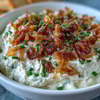 Creamy caramelized onion dip with sour cream and fresh chives, served with crispy potato chips and colorful crudités.  